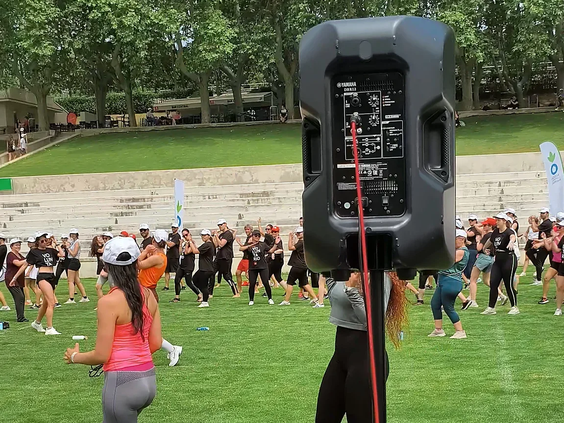 Altavoz en trípode orientado hacia una clase colectiva en un campo de césped